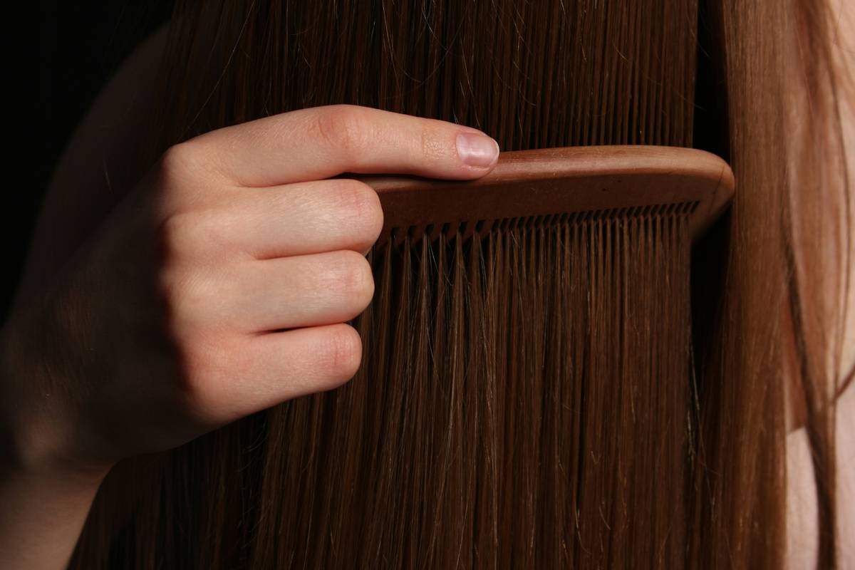 Woman applying women’s hair gel to damp hair while styling in bathroom mirror